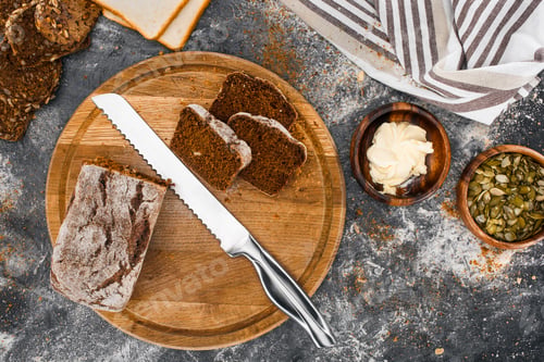 Preview: top view of bread and knife on cutting board and bowls with butter and pumpkin seeds on black slate