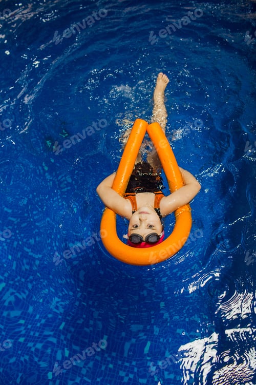 Preview: child girl swimming on her back with a pool noodle in swimming pool, top view floating.