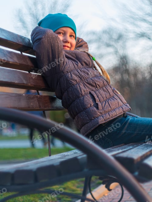 Preview: Happy girl with long braided hair portrait in spring park sits on a tree on sunset outdoor.