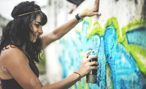 A young woman spray painting graffiti onto a wall.