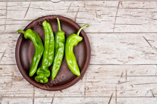 Preview: Fresh green raw peppers on brown ceramic plate on rustic wooden table background.