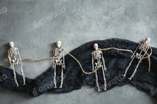 Preview: Halloween decorations, toy skeletons on black fabric, top view from above