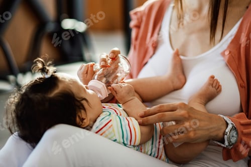 Preview: Baby girl drinking water while relaxing in mother's lap.