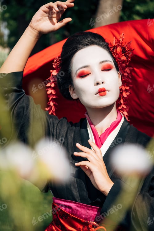 Preview: selective focus of tree branches and dancing geisha with red cloth on background in sunlight