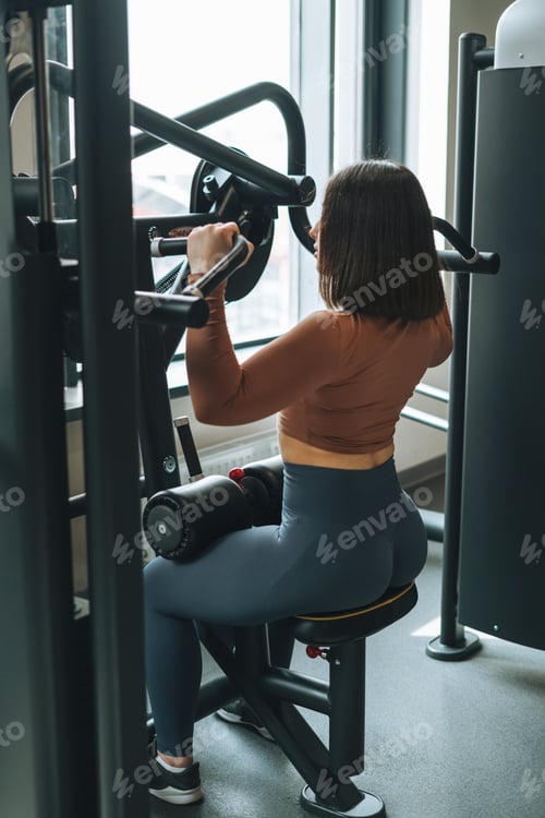 Preview: Young fitness brunette woman training for back muscles equipment at gym