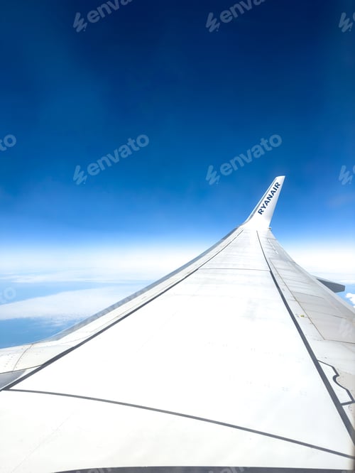Preview: View from an airplane window showing the wing of a Ryanair aircraft flying over the clouds