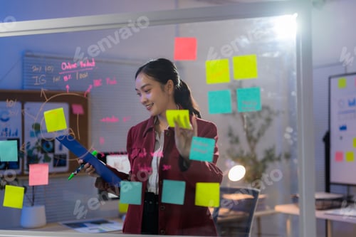 Preview: Young professional sticking notes on a glass wall, working late in the office on a new project