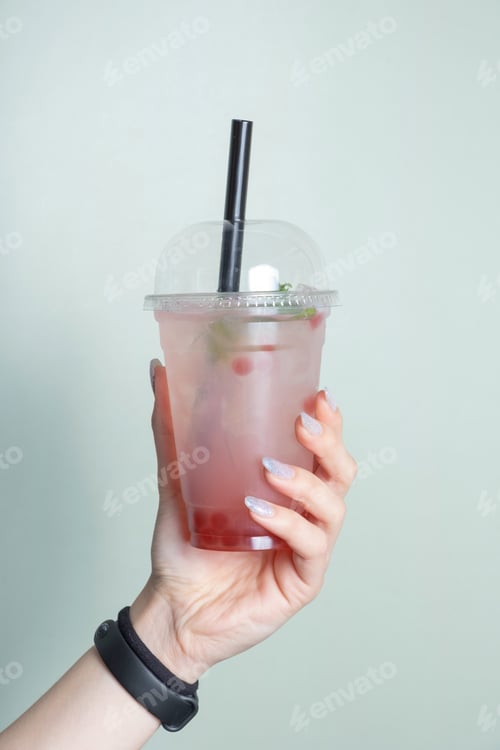 Preview: Plastic glass with bubble tea and ice in female hand. Trendy cold summer drink
