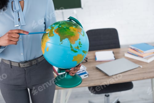 Preview: Cropped view of african american teacher pointing at globe with pencil