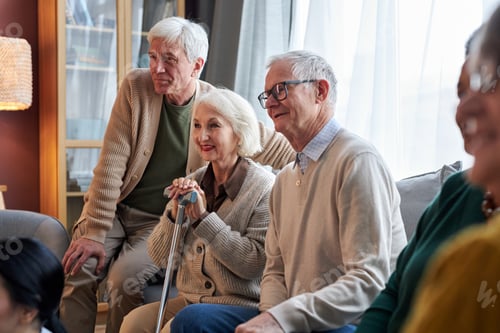 Preview: Smiling senior people watching TV in retirement home together sitting on sofa