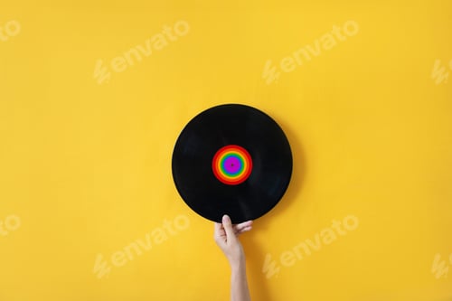Preview: Female hand holding a plate with LGBT symbol on a yellow background