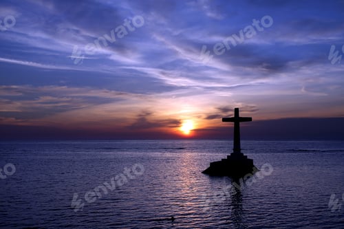 Preview: Silhouette of Christian cross on the stone thumb in the lake against a bluish sunset sky