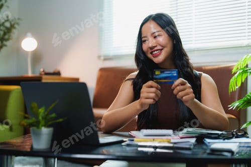 Preview: Smiling asian freelancer using credit card for online shopping at home office