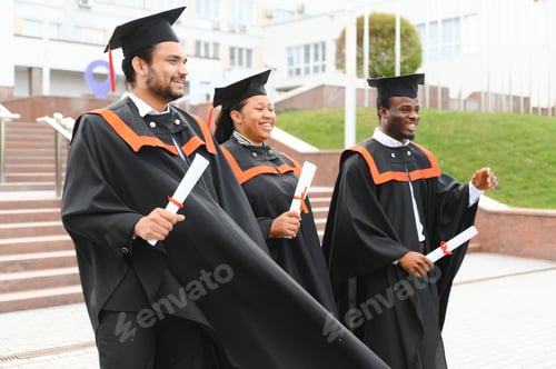 Preview: Group of happy smiling multicultural people in graduation gowns and caps with diplomas in hands