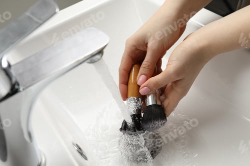 Preview: Woman washing makeup brushes under stream of water in sink, closeup