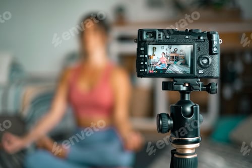 Preview: Young woman exercising at home doing pilates and recording at her with digital camera to teach