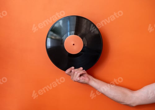 Preview: Male hand holding vinyl record on background of orange wall.