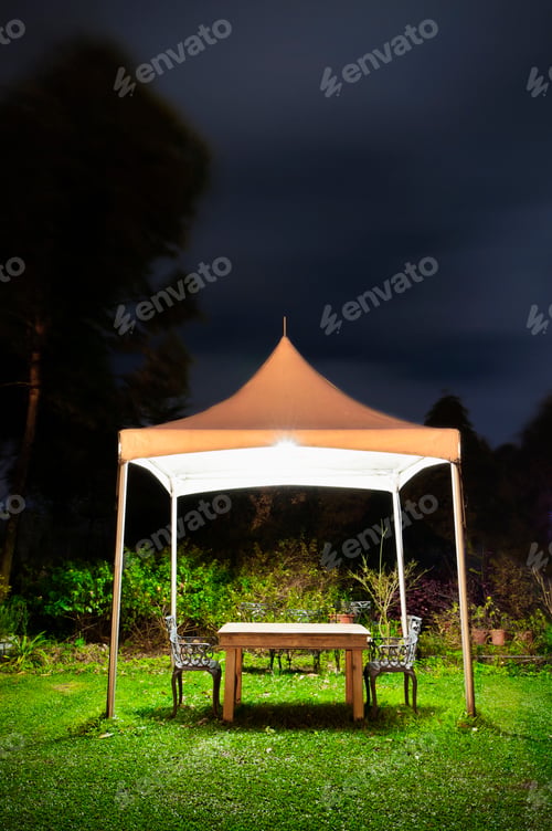 Preview: A small gazebo in a garden, a table and seat and lights at night