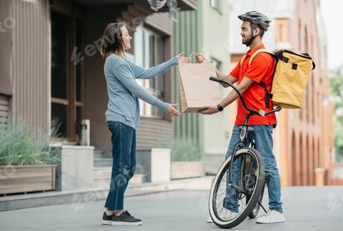 Preview: Courier with bicycle delivered shopping bag to client. Smiling girl takes bag from man in helmet