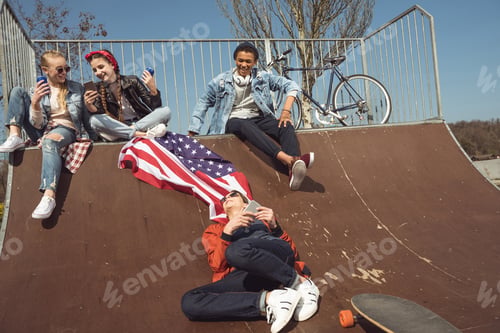 Preview: teenagers having fun with american flag in skateboard park, hipster students concept