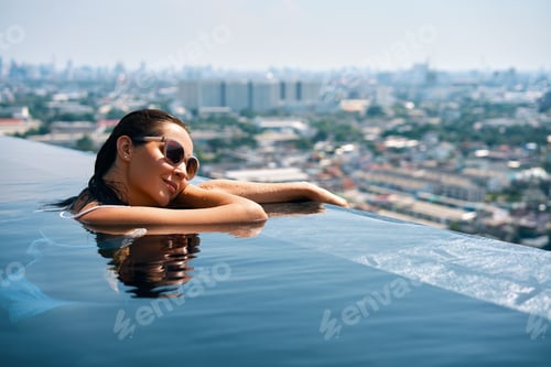 Preview: Young woman relax on the edge of the roof top swimming pool