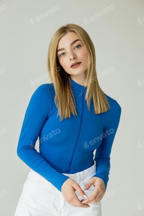 Preview: blonde and stylish woman in blue turtleneck looking at camera isolated on grey