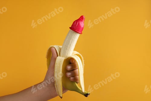 Preview: Woman holding banana in condom on orange background, closeup and space for text. Safe sex concept