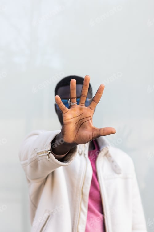 Preview: Black man covering face and showing stop gesture in city street