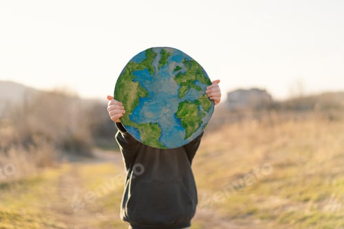 Preview: Little boy holding planet in hands against green spring background. Earth day