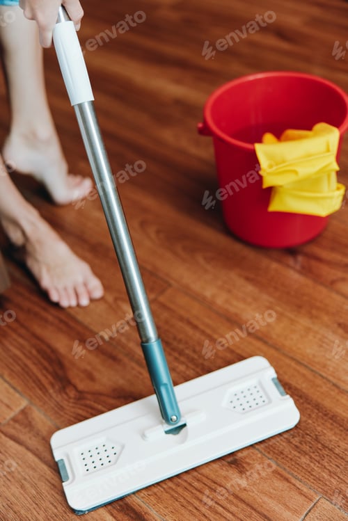 Preview: Woman using mop to clean wooden floor with buckets of water and cleaning solution nearby