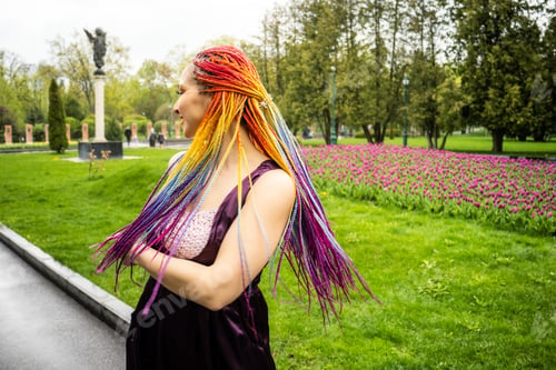 Preview: A girl in a purple dress and with rainbow long braids laughs and jumps in green blooming from the