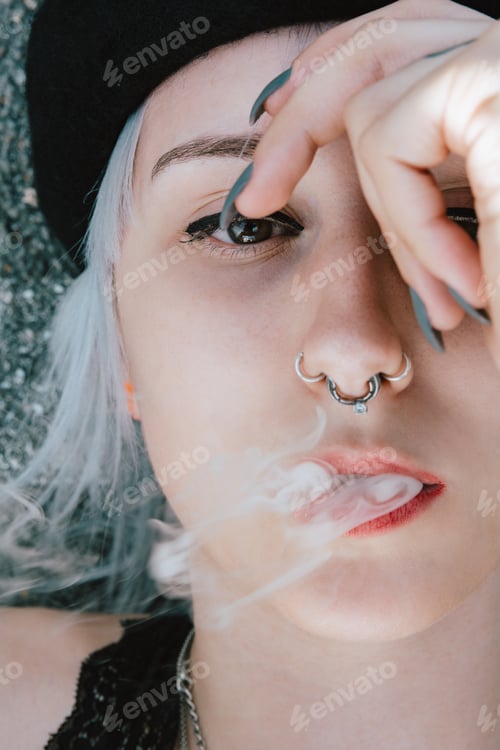 Preview: Portrait of a blonde female lying on the ground and smoking with her hand on her face