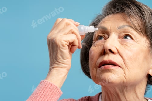 Preview: Elderly woman applying eye drops looking up on blue background