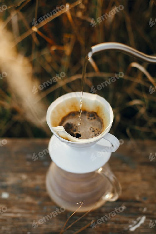 Preview: Hand pouring hot water from steel kettle in glass flask dripper with filter