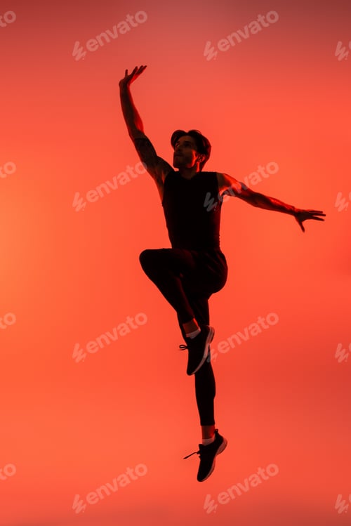 Preview: Athletic sportsman in black sportswear jumping on red background