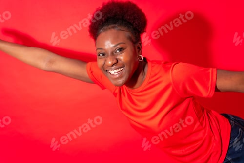 Preview: Young african american woman isolated on a red background smiling and dancing, studio shoot