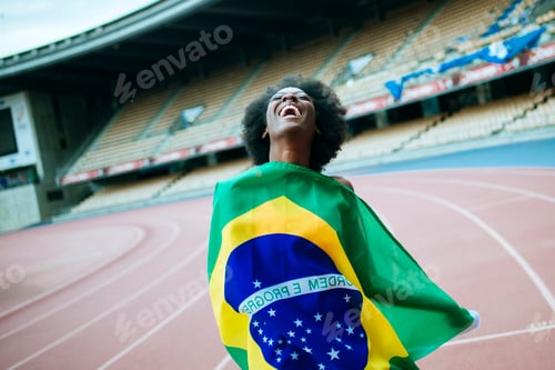 Preview: Brazilian athlete celebrating victory with national flag in stadium
