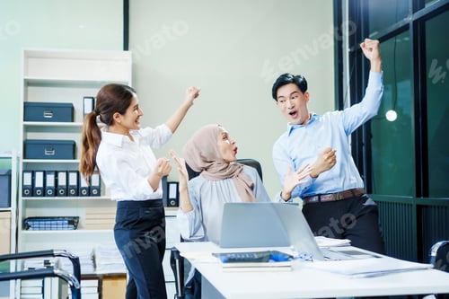Preview: A Muslim businesswoman and an Asian woman sit with a middle-aged businessman at a desk a laptop