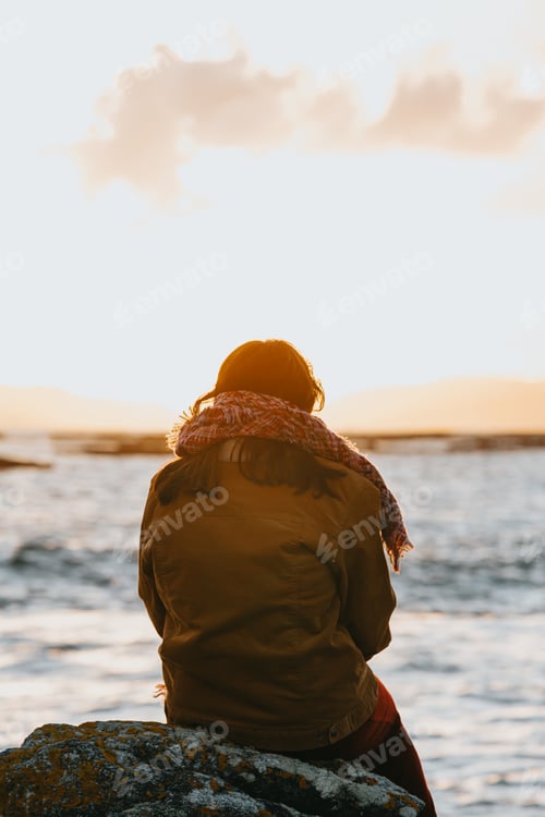 Preview: A woman thinking about something in front of a colorful sunset and the ocean
