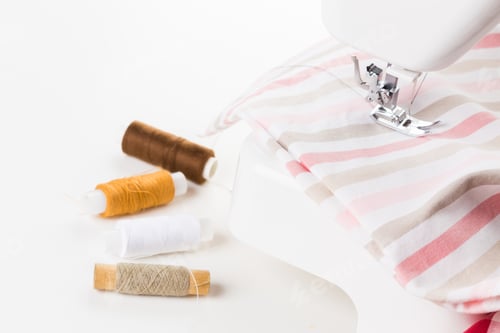 Preview: Sewing machine with colorful threads and striped fabric on a work surface at home