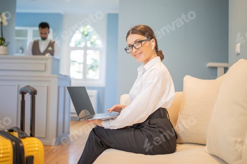 Preview: Businesswoman working on laptop in hotel lobby with a friendly staff member