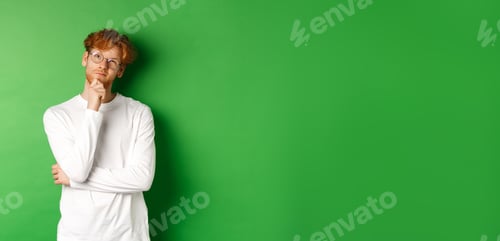 Preview: Thoughtful redhead man in glasses making choice, looking up and thinking, standing over green