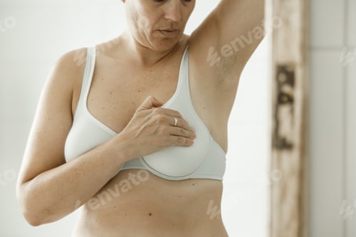 Preview: Breast cancer awareness day, woman in front of mirror checking her breasts at home