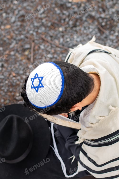 Preview: Photo taken from above of a Jewish man with kippah and taltit, performing a religious prayer ritual.