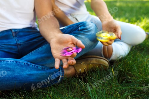 Preview: Young girl and boy playing with fidget spinners in the park. stress relieving toy. Sunny summer day.