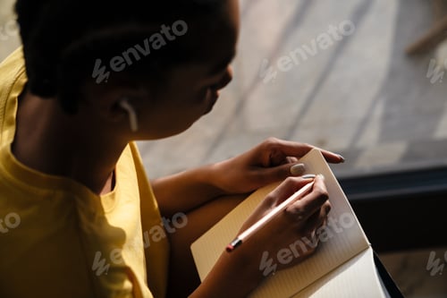 Preview: Happy african american girl in earphones writing down notes