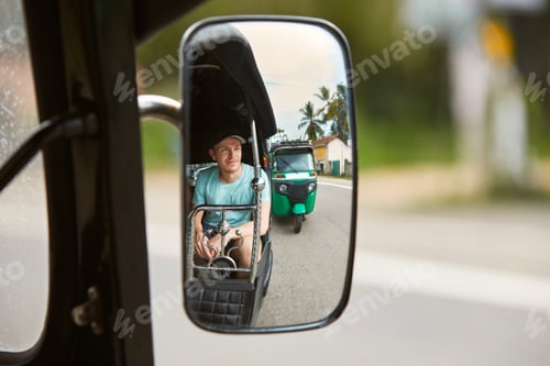 Preview: Man traveling by tuk tuk. Reflection of tourist in mirror of three wheeled motorcycle in Sri Lanka.