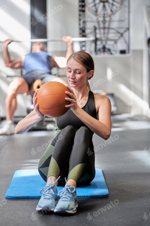 Preview: Sporty woman exercising with ball on fitness mat at the gym.
