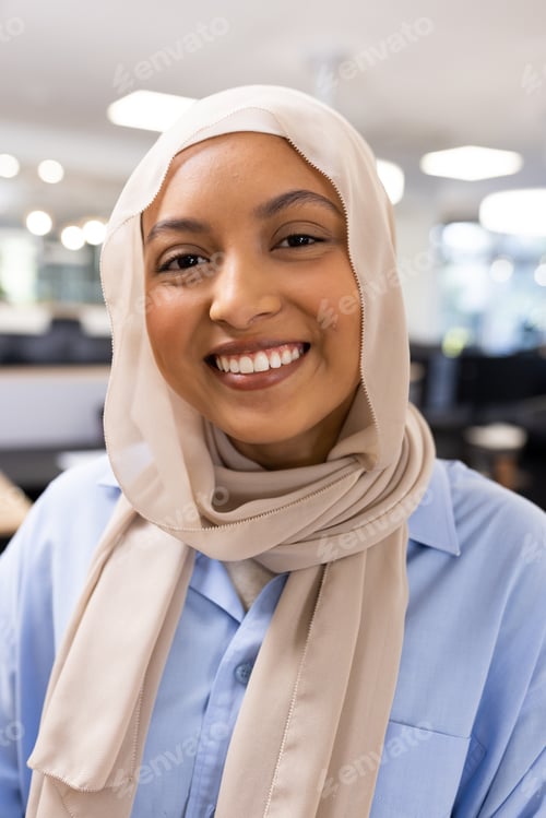Preview: Vertical image of happy middle-eastern businesswoman in hijab looking at camera in office