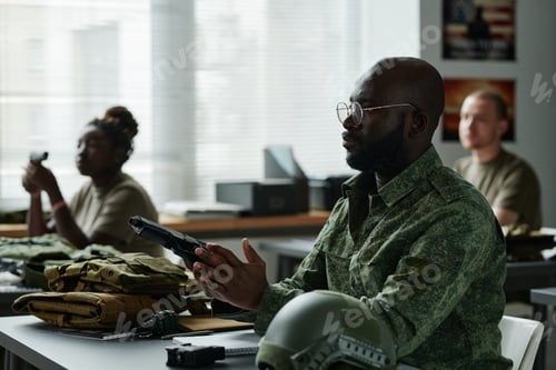 Preview: Young serious African American man in eyeglasses and uniform loading gun